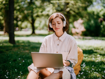 Drau sitzt im Park mit Laptop und Kopfhörern. 